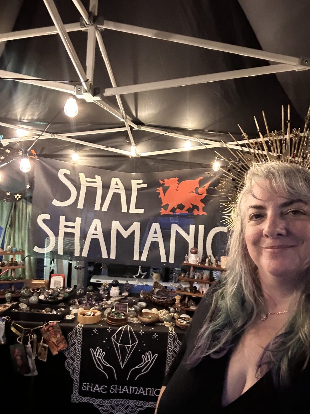 Shae smiling in a gold spiked halo headdress in front of her gemstone booth